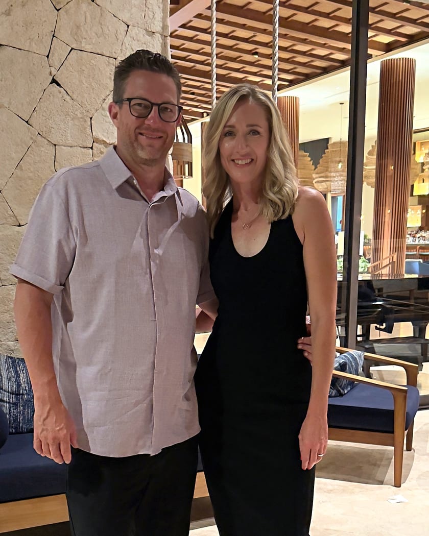 Clark and Carrie Sell, standing together in a hotel lobby, both smiling.
